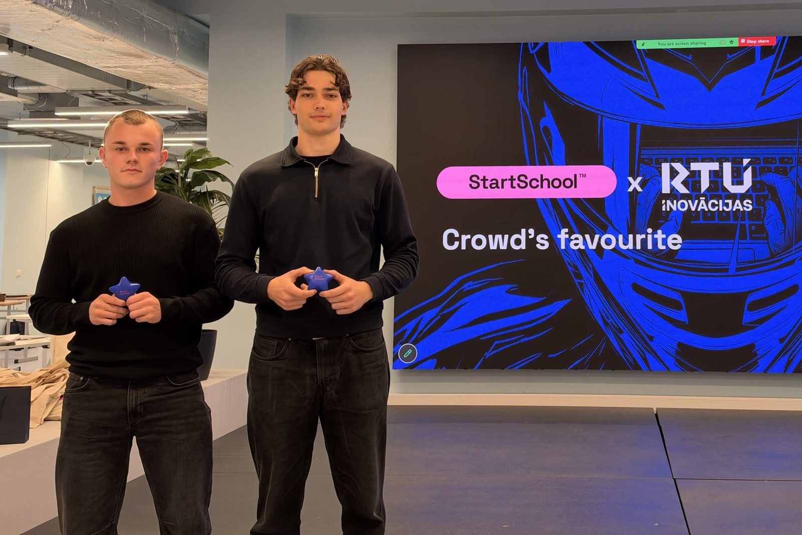 Erlens Toms Rukers and Rūdolfs Šuklais on the StartSchool x RTU Inovācijas stage, Crowd’s favourite on the screen behind them